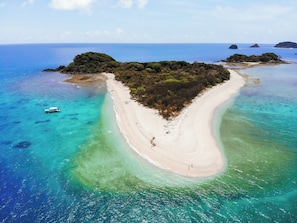 An aerial view of a beach with clear turquoise waters, a sandy shoreline, and a boat in the water. - Hidden Gem • 3BR Home in Cairns
• Close to Airport, CBD & Attractions (Edge Hill)