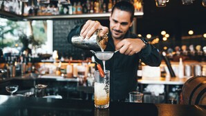 Een barman maakt een drankje met een shaker en een zeef.