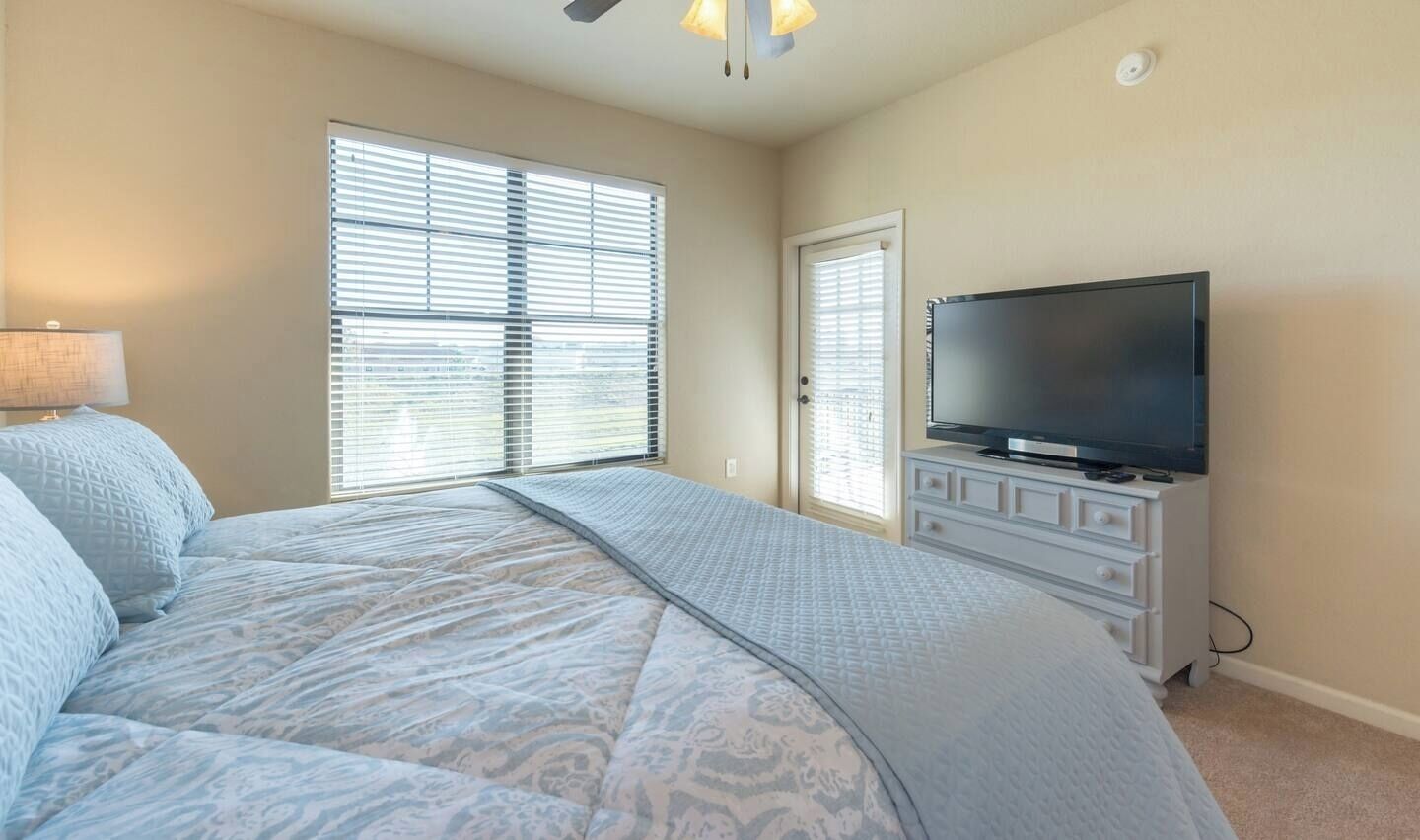 A bedroom with a large bed, a television on a dresser, and a window with blinds.