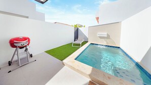 Ein moderner Poolbereich im Freien mit Whirlpool, Grill und einer kleinen Rasenfläche.