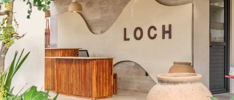 En receptionsdisk med et træribbedesign, en stor keramisk vase og en væg med navnet "LOCH" i store bogstaver.