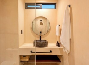 A bathroom with a round mirror, a wooden sink, a towel rack, and a small window. - Loch Collection Tulum (Tulum)