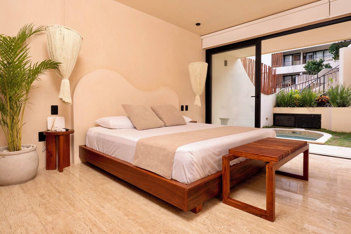 A modern bedroom with a wooden bed, a large potted plant, and a view of the outdoor area.