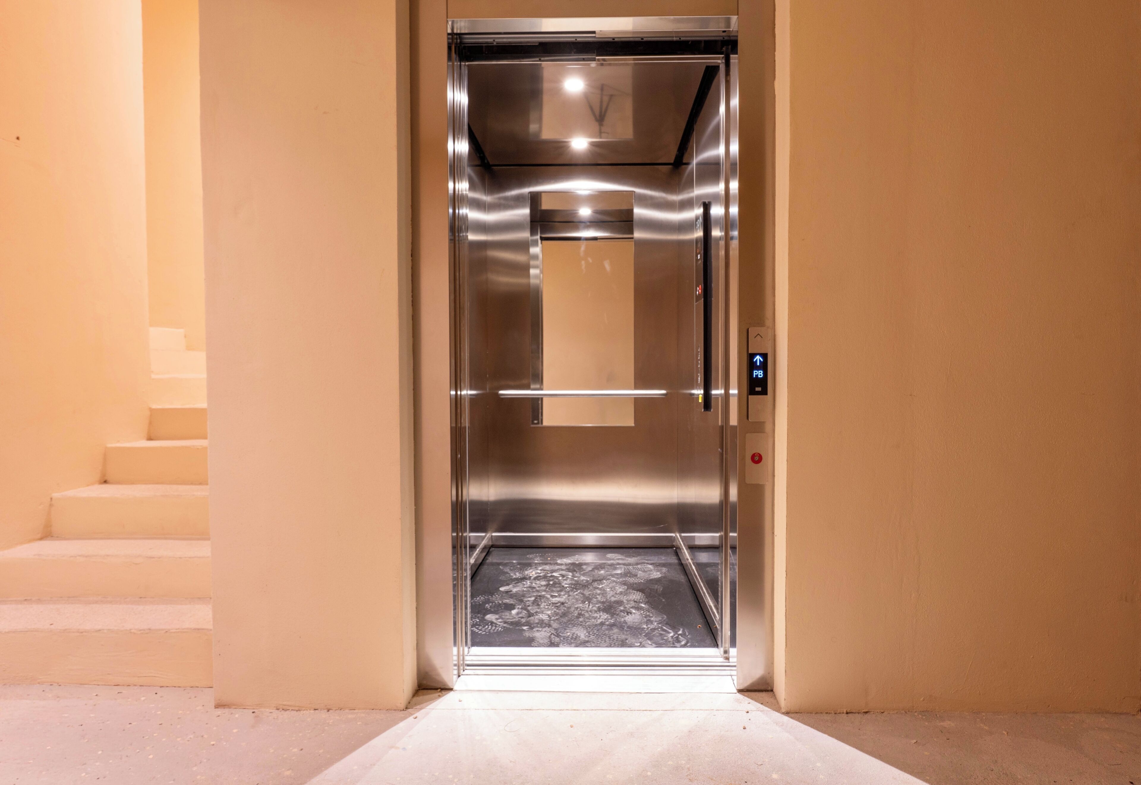 Ascensore con interni metallici, un pannello di controllo e una porta in vetro.