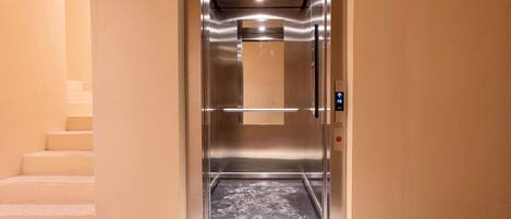 Ascensore con interni metallici, un pannello di controllo e una porta in vetro.