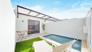 Un área de piscina moderna al aire libre con un vidrio, una pequeña mesa con sillas y césped artificial verde.