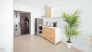 Una cocina moderna con horno empotrado, un lavamanos y una cafetera. Hay una planta en maceta y una puerta corrediza que da a otra habitación.