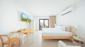 Una habitación de hotel moderna con cama, mesita de noche, lámpara y un rincón de comedor con mesa y sillas.