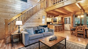 Ein Holzinterieur mit einer Treppe, einem Wohnbereich mit Sofa, Couchtisch und einer Küchenzeile mit Holzmöbeln.