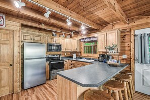 A wooden cabin interior with a kitchen featuring a refrigerator, stove, microwave, and wooden cabinets. - Serene Retreat w/ Hot Tub, Deck & Pool Table Between Pigeon Forge & Gatlinburg (Sevierville)