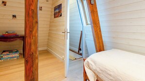 A room with wooden walls, a slanted ceiling, a bed, a desk with books, and a small window. - Apartment Cigale by Interhome (Deauville-Trouville)