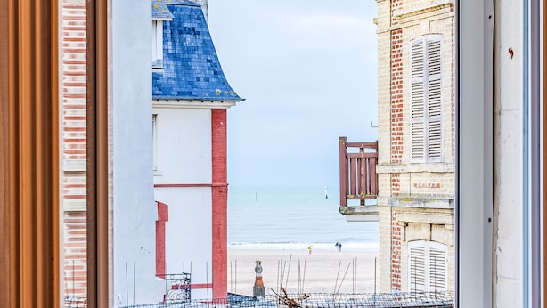 A view through a window of a building with a blue roof and a brick facade, overlooking a beach. - Apartment Cigale by Interhome (Deauville-Trouville)