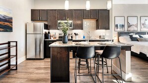 A modern kitchen with dark cabinets, stainless steel appliances, and a central island with bar stools. - The Golden Retreat- Mountain Views + Private Patio (Golden)