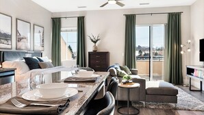 A modern hotel room with a dining area, a sofa, and a balcony with curtains. - The Golden Retreat- Mountain Views + Private Patio (Golden)