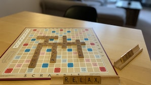 Een Scrabble spelbord op een houten tafel met een Scrabble letterrek ernaast.