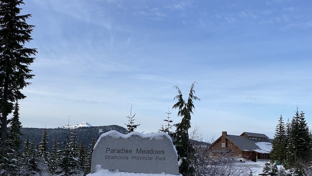 Een stenen bord met de tekst 'Paradise Meadows Strathcona Provincial Park', omringd door met sneeuw bedekte bomen en een gebouw op de achtergrond.