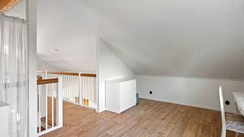 Ein geräumiges Dachzimmer mit Holzboden, weißen Wänden und einer Holztreppe.