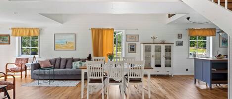 A spacious living area with a dining table, a sofa, and a staircase leading to an upper level.