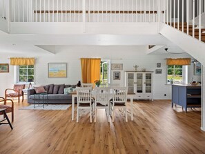 A spacious living area with a dining table, a sofa, and a staircase leading to an upper level.