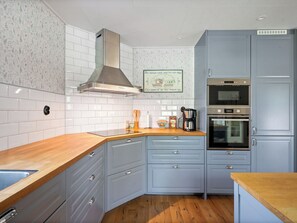 A kitchen with white tiled backsplash, a stainless steel range hood, a double oven, and light blue cabinets.