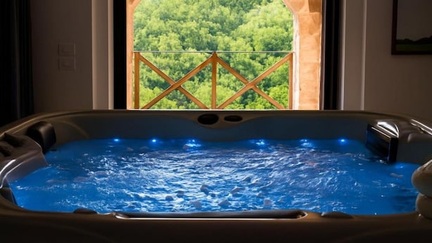 Ein Whirlpool mit Blick auf einen Wald durch ein Fenster mit steinbogiger Einfassung.