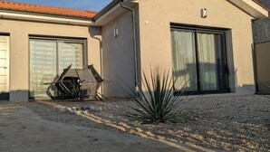 Une maison moderne avec un garage, une terrasse agrémentée d’une petite plante et une allée gravillonnée.