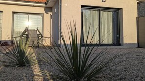 Une maison moderne à l’extérieur beige, avec un toit en tuiles et une grande porte-fenêtre coulissante. On aperçoit deux plants d’agave au premier plan.