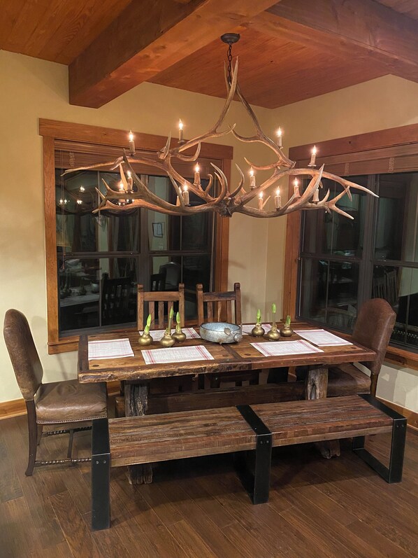 A dining table with a chandelier, wooden chairs, and a window with blinds. - The Hollows at Lake Travis Retreat (Jonestown)