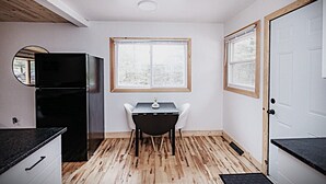 Eine kompakte Küche mit Esstisch, einem schwarzen Kühlschrank und einem Fenster mit Blick auf Bäume.