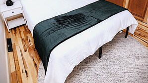 Ein Schlafzimmer mit Holzboden, einem Bett mit weißer Bettwäsche, einer dunkelgrünen Decke, einem Nachttisch mit Lampe und einem Kleiderschrank.