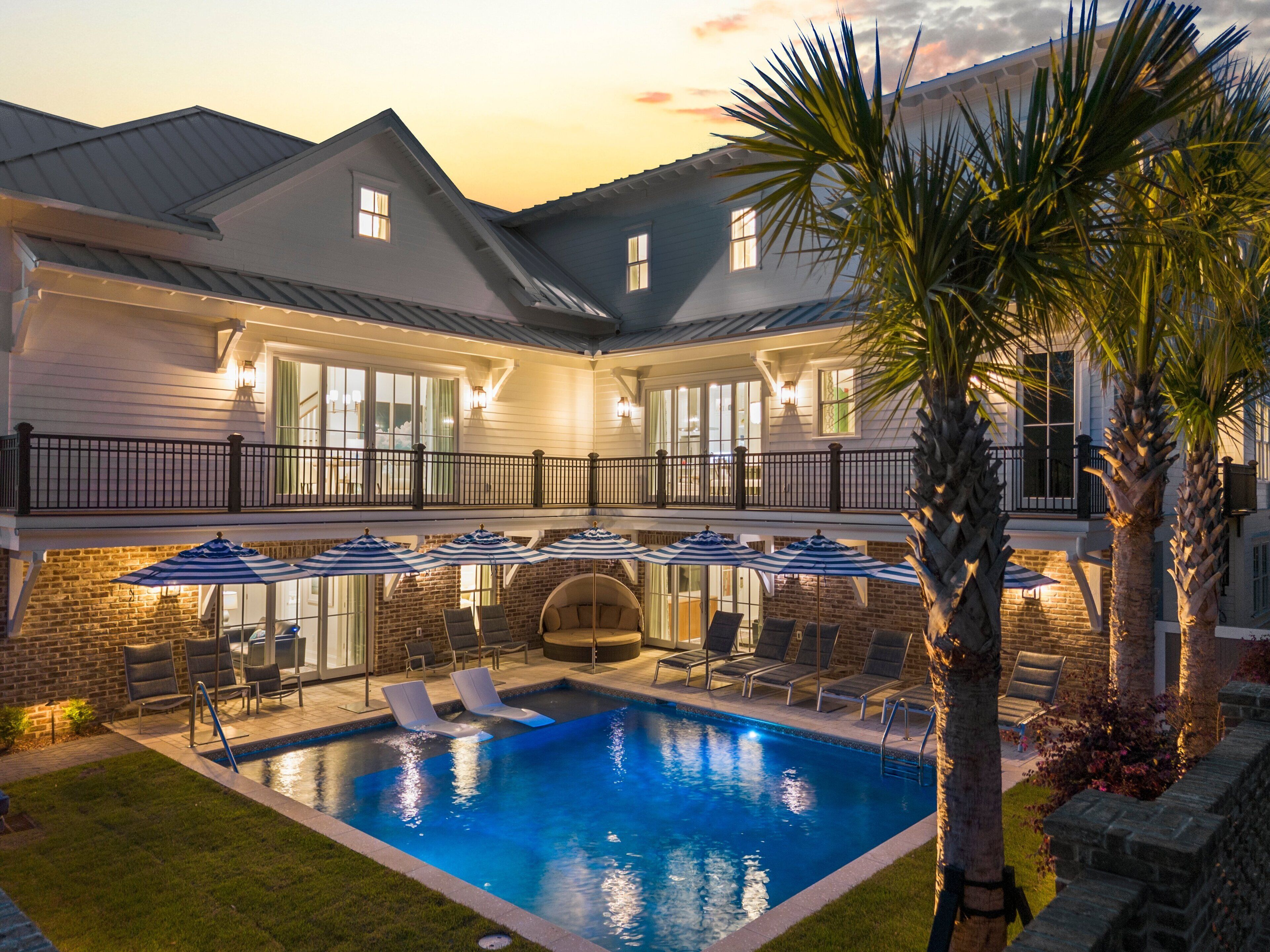 Une maison à deux étages avec une piscine, un espace salon extérieur et un balcon.