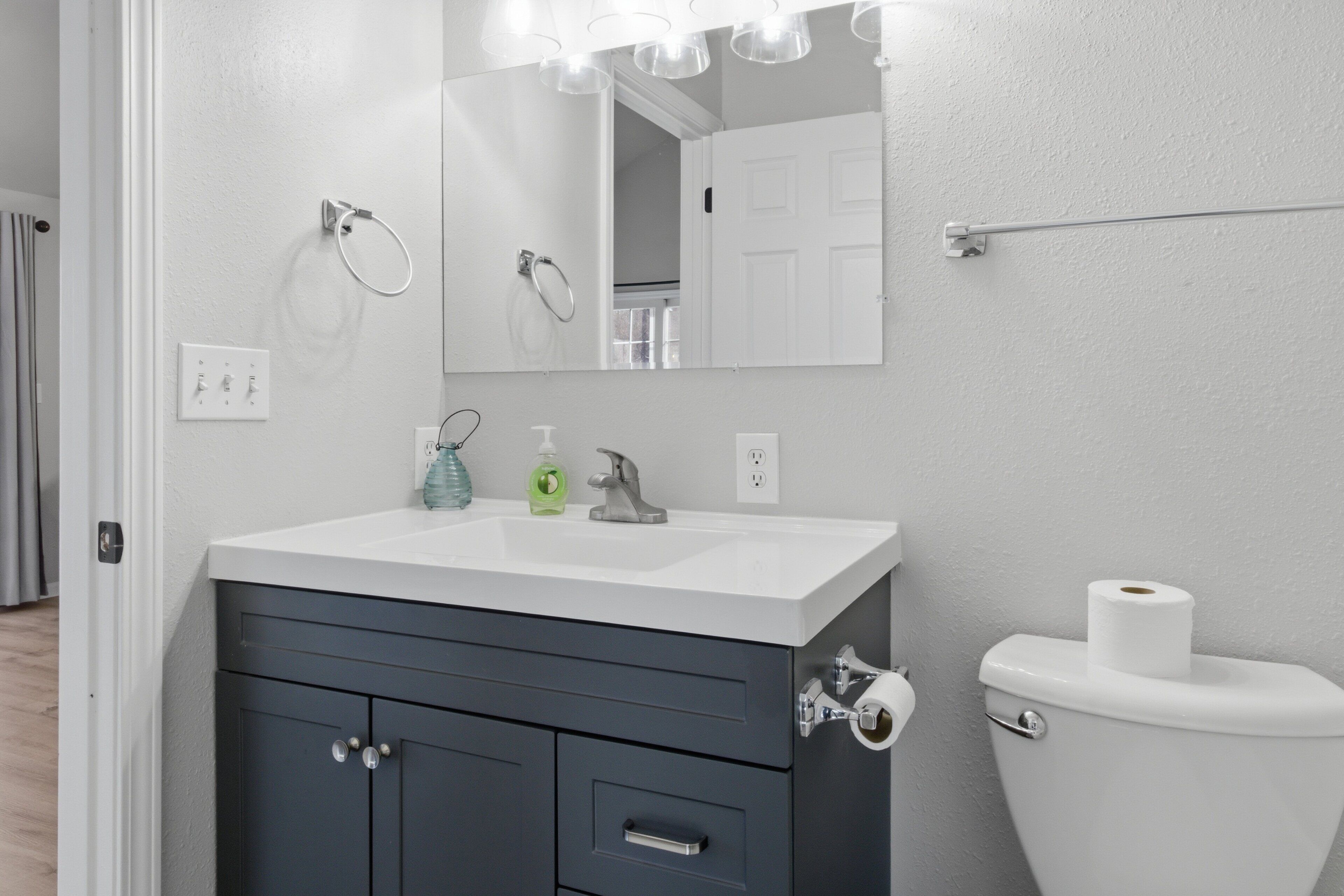A bathroom with a white sink, dark cabinets, a mirror, and a toilet.