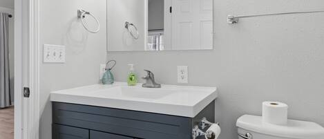 A bathroom with a white sink, dark cabinets, a mirror, and a toilet.