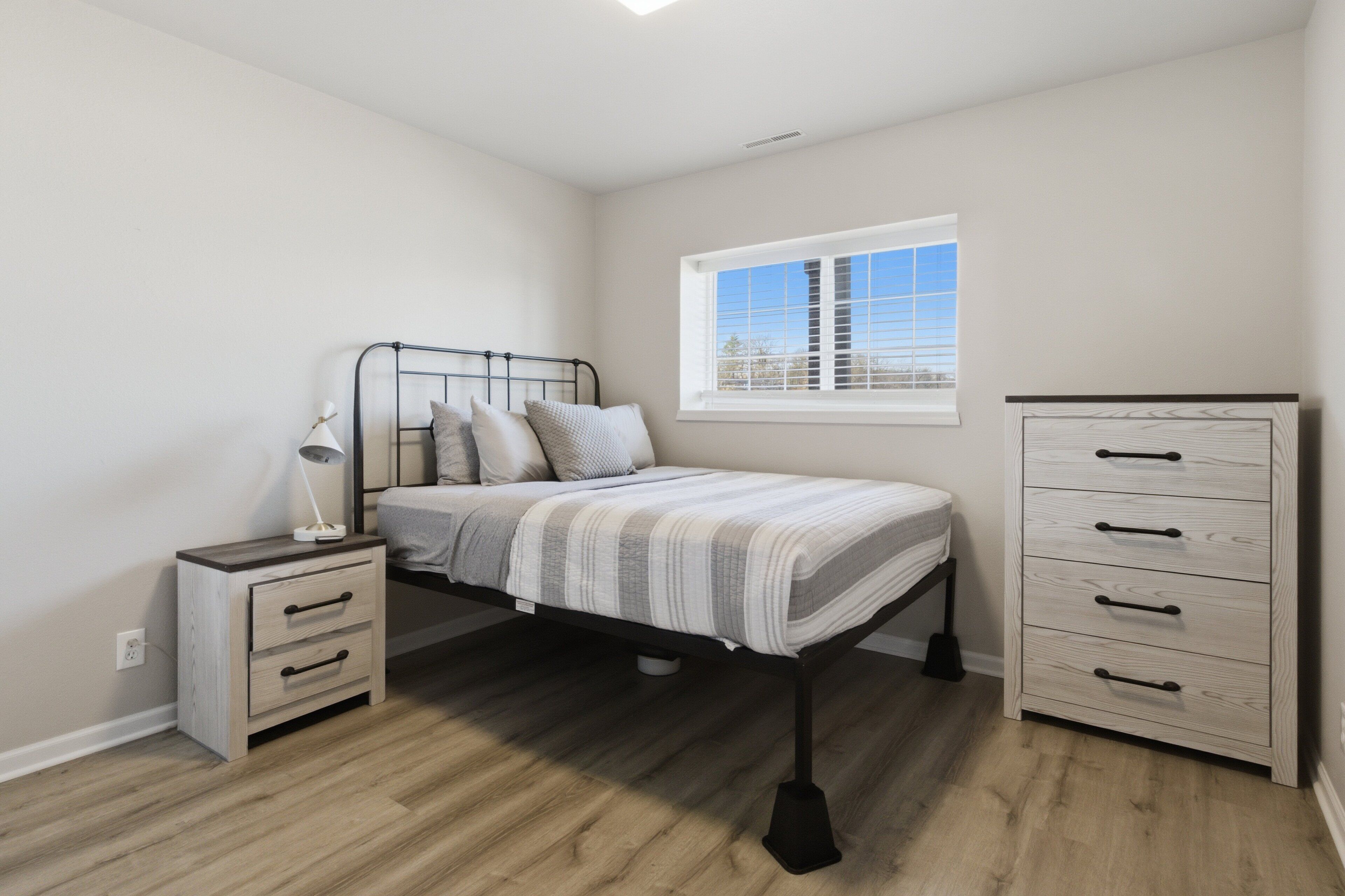 Un dormitorio con cama, mesita de noche, cómoda y ventana.