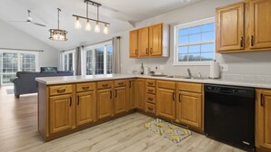 A modern kitchen with wooden cabinets, a dishwasher, and a large window. - Lakefront Home in Osage Beach 28mm at Miller's Landing (Osage Beach)