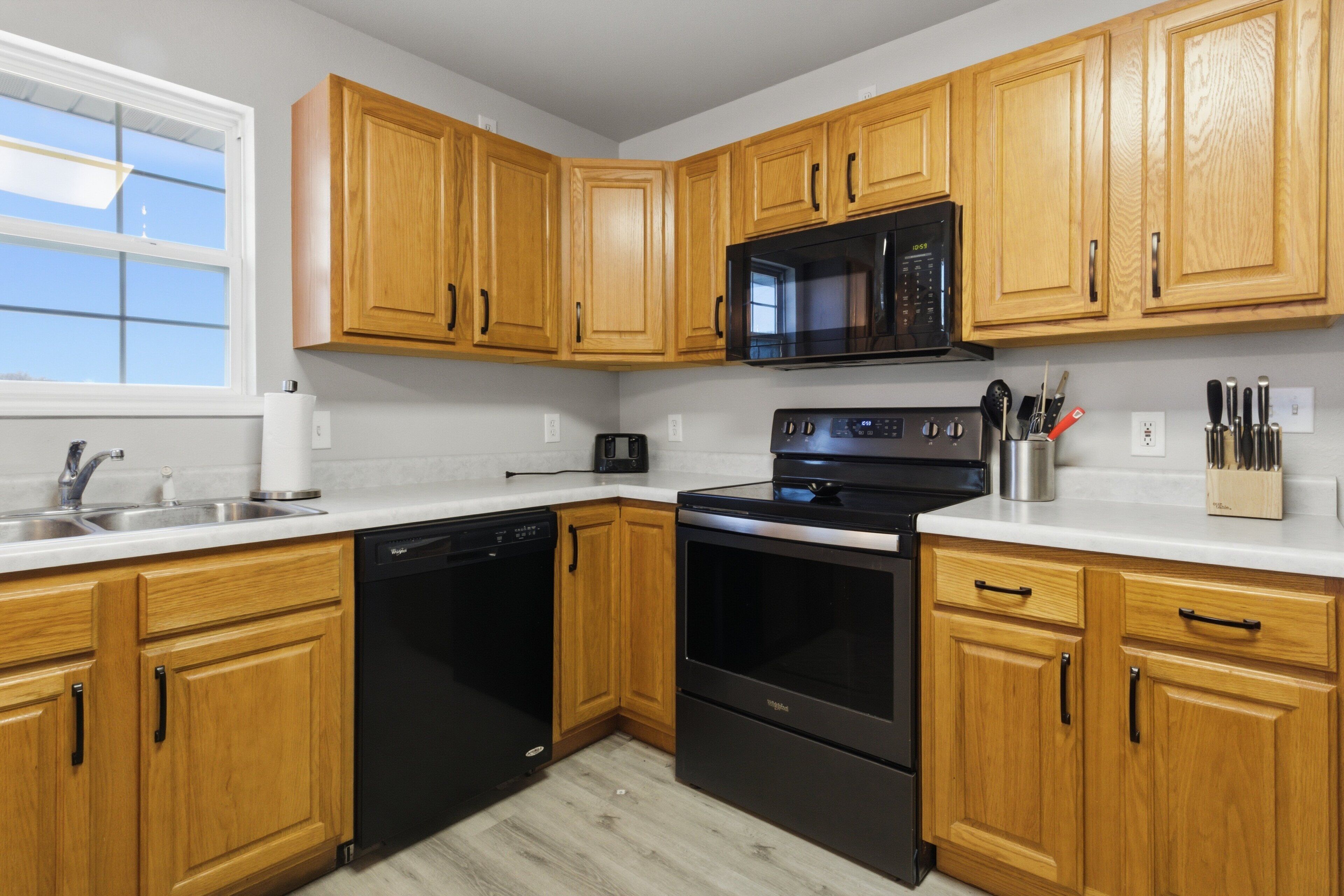 A modern kitchen with wooden cabinets, a black microwave, a dishwasher, and an oven.