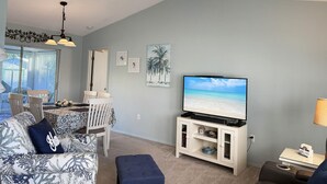 A living room with a ceiling fan, a TV, a dining area with chairs and a table, and a beach-themed painting on the wall. - Peaceful 3BR Villa – Near Beaches & Golf (Englewood)
