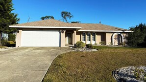 A single-story house with a garage, a front door, and a small front yard with a lawn and a few shrubs. - Peaceful 3BR Villa – Near Beaches & Golf (Englewood)