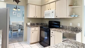 A compact kitchen with light wood cabinets, a built-in microwave, a stove, and granite countertops. - Peaceful 3BR Villa – Near Beaches & Golf (Englewood)