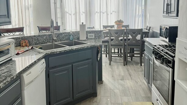 Une cuisine moderne dotée d’un îlot central, de meubles de rangement aux couleurs sombres, d’un coin repas avec une table et des chaises, et offrant une vue sur l’extérieur grâce à de grandes fenêtres.