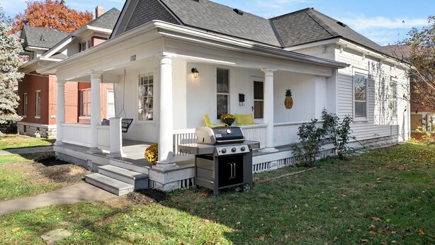 A two-story house with a covered porch, a grill, and a small garden.