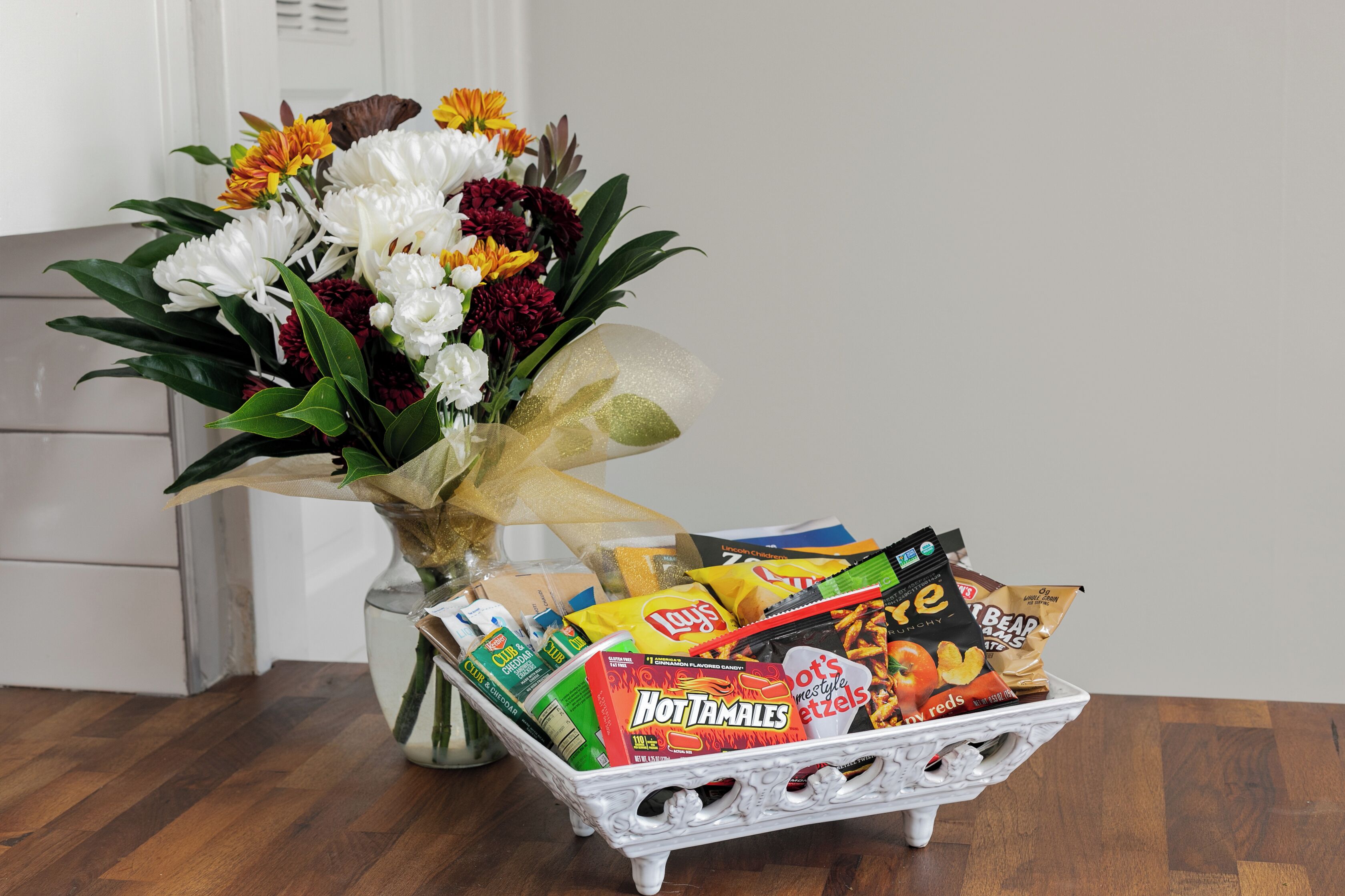 A table with a vase of flowers and a basket of snacks.