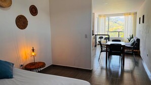 Habitación de hotel con cama, una mesita de noche con lámpara y vistas al balcón con mesa y sillas.