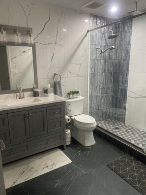 Un baño moderno con tocador de mármol, inodoro y zona de ducha.