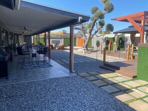 Un patio techado con mobiliario exterior, una pérgola y un jardín con grava y piedras.