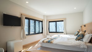 Une chambre à coucher moderne avec un lit, un téléviseur fixé au mur et deux fenêtres avec des rideaux.