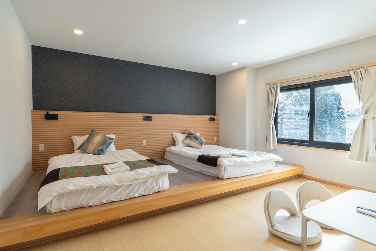 Quarto moderno com duas camas, uma escrivaninha e uma janela com cortinas.