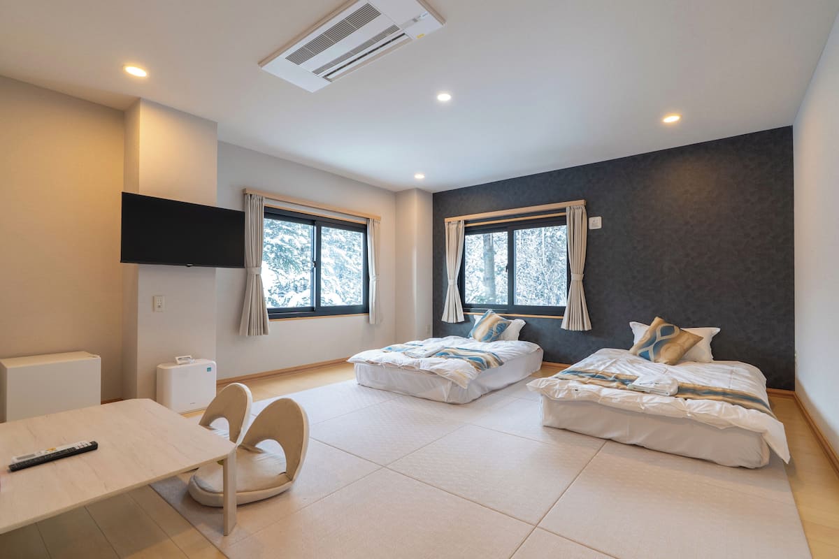 Quarto de hotel moderno com duas camas, uma escrivaninha e uma televisão.