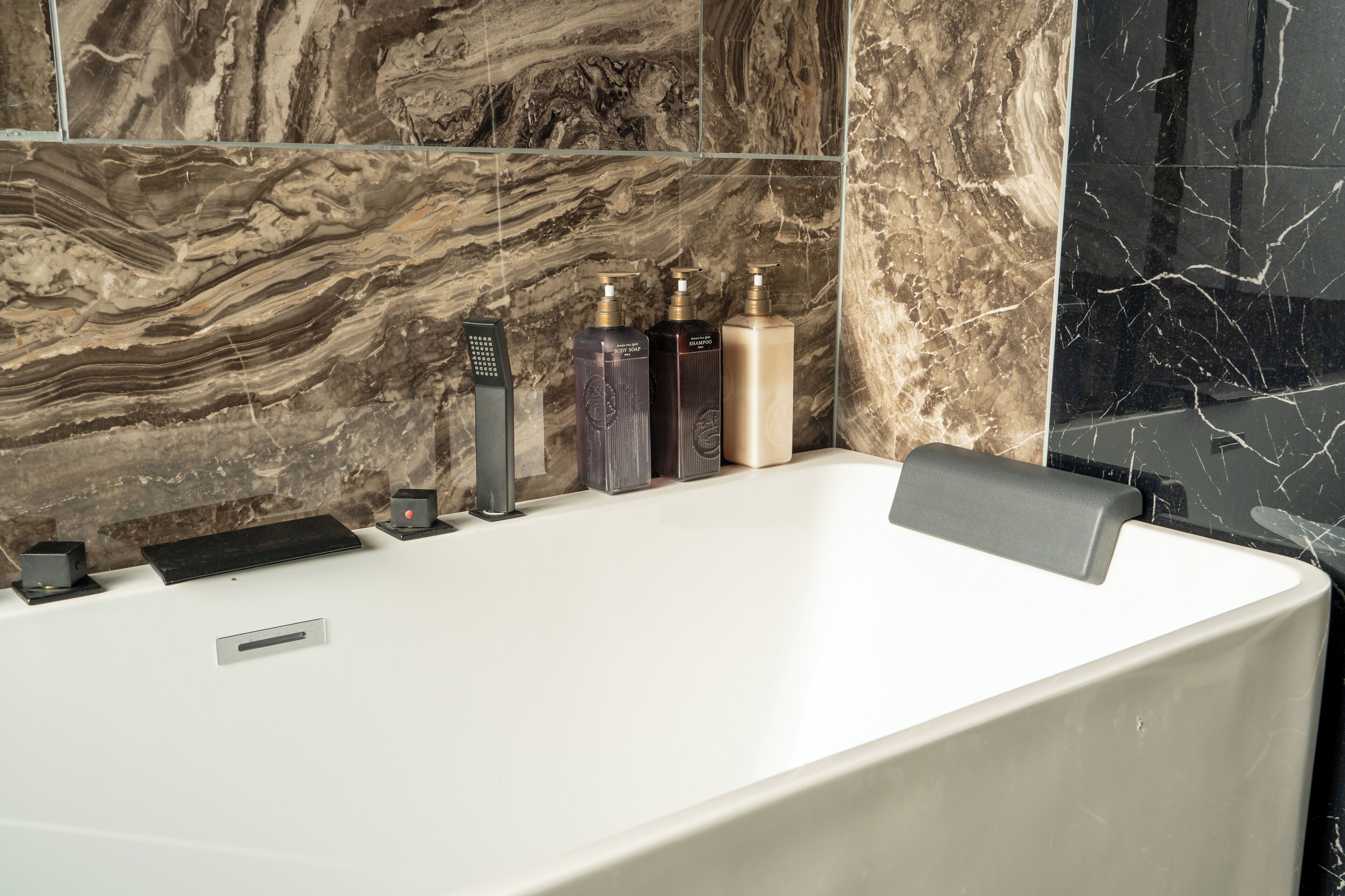 Un baño moderno con pared de mármol, una bañera blanca y tres artículos de tocador a un lado.