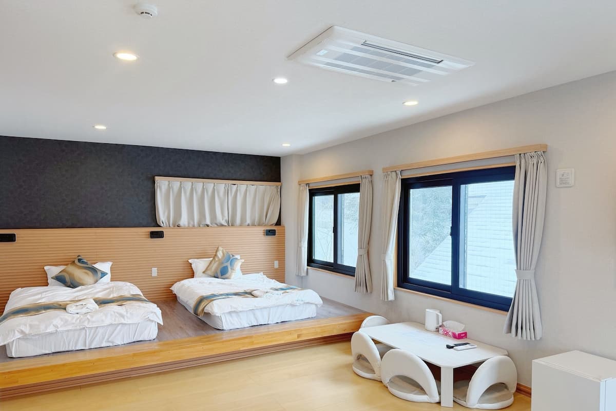 Quarto de hotel moderno com duas camas, uma mesinha e uma cadeira.